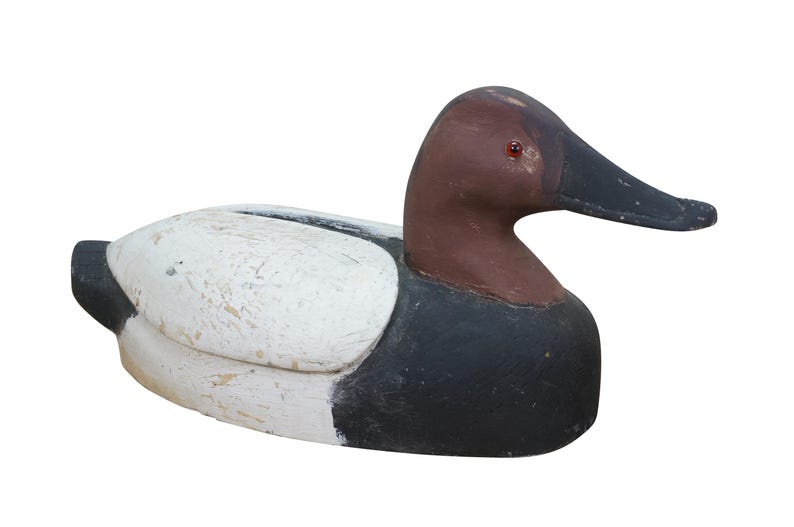 May include: A wooden duck decoy with a white body, black and brown accents, and a black beak. The decoy has a weathered appearance, suggesting it is vintage or antique. The duck is a decorative item.