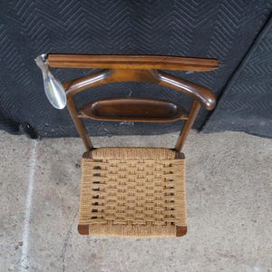 May include: A vintage wooden valet chair with a woven seat. The chair has a curved back and a bar for hanging clothes. A metal shoe horn hangs from the top. The chair is made of dark wood.