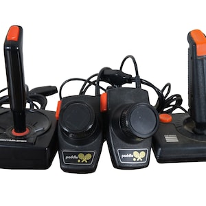 May include: Four vintage Atari game controllers, including a joystick and three paddle controllers. The joystick is black with an orange button and the text "PONGMASTER" on the base. The paddle controllers are black with orange buttons and the text "paddle" on the base.