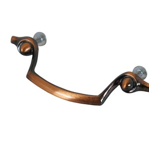 May include: A copper-toned cabinet pull with a decorative, curved design. The pull has a smooth, polished finish and is attached to a white background.