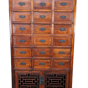 Pode incluir: Um arm&aacute;rio de madeira antigo, com v&aacute;rias gavetas e uma sec&ccedil;&atilde;o inferior com portas. O arm&aacute;rio &eacute; castanho quente, com puxadores de metal escuro e pain&eacute;is decorativos em treli&ccedil;a. Altura aproximada: 180 cm.