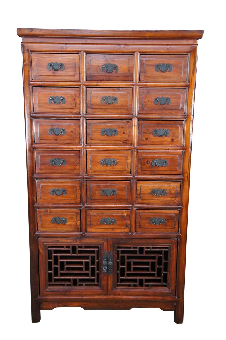Pode incluir: Um arm&aacute;rio de madeira antigo, com v&aacute;rias gavetas e uma sec&ccedil;&atilde;o inferior com portas. O arm&aacute;rio &eacute; castanho quente, com puxadores de metal escuro e pain&eacute;is decorativos em treli&ccedil;a. Altura aproximada: 180 cm.