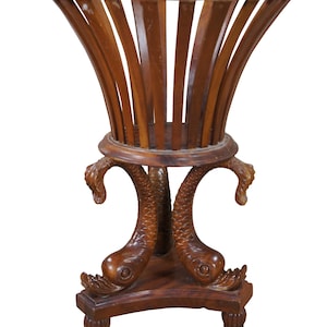 May include: A wooden plant stand with a round top and a decorative base. The base is carved to resemble two fish with their tails intertwined. The stand is made of dark brown wood.