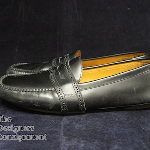 May include: A pair of black leather loafers with a decorative stitch detail. The loafers have a pointed toe and a low heel.