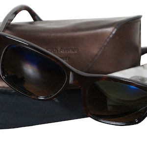 May include: Brown tortoise shell sunglasses with dark lenses and a brown leather case. The sunglasses are resting on a black fabric pouch with a drawstring.