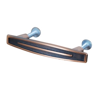 May include: A copper-colored cabinet pull with a black inlay and two silver screws. The pull has a slightly curved shape.