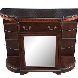 May include: A dark wood semi-circular console table featuring a top glass surface, a central drawer with two metal pulls, and a single cabinet door with a mirrored front panel. The unit includes two curved glass shelves on each side of the cabinet.