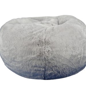 May include: A large, round beanbag chair in a soft, light gray color. The beanbag has a plush, faux fur texture, with a slight gradient of darker gray at the base. The chair is designed for comfortable seating.