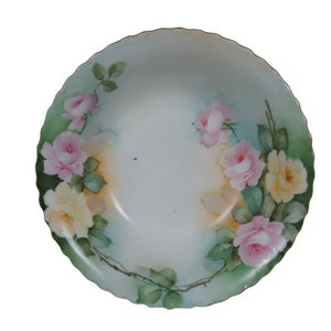 May include: A white porcelain bowl with a scalloped edge, decorated with a floral design of pink and yellow roses with green leaves on a light blue background.