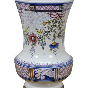 May include: White ceramic vase with a flared shape, adorned with colorful floral and leaf patterns. The vase features a square top and a decorative base with a blue, purple, and brown design. The vase is approximately 10 inches tall.