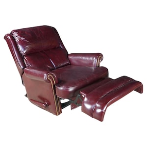 May include: A deep burgundy leather recliner chair featuring a high backrest, padded armrests, and an extended footrest. The front edges of the armrests are accented with a row of small, metallic brass-colored nailhead trim studs.