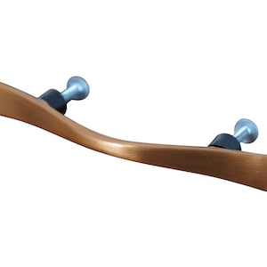 May include: A curved, brushed copper cabinet pull with black screw covers. The pull has a modern, minimalist design.
