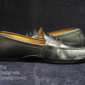 May include: A pair of black leather loafers with a penny strap detail. The loafers have a stitched edge and a slightly worn appearance.
