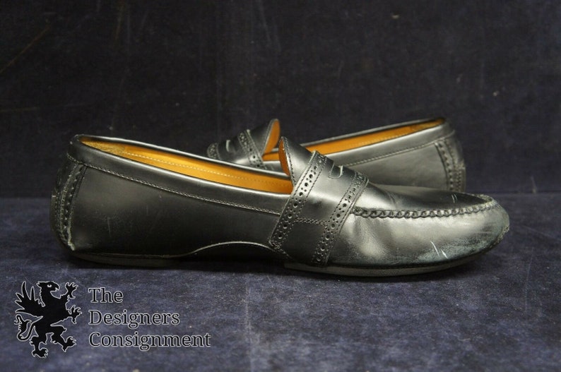 May include: A pair of black leather loafers with a penny strap detail. The loafers have a stitched edge and a slightly worn appearance.