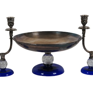 May include: A silver serving set with a blue glass bowl and two candle holders. The bowl has a round base with a clear glass orb and a blue glass base. The candle holders have a similar design with a clear glass orb and a blue glass base.