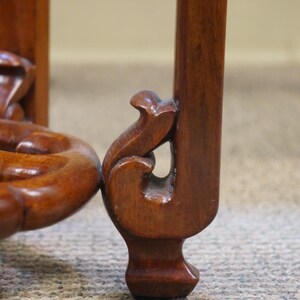 May include: Close-up of a wooden furniture leg with ornate carved details. The leg is a rich, dark brown color, with a curved design at the base and a decorative element near the top. The wood grain is visible.