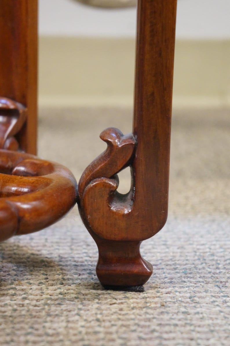 May include: Close-up of a wooden furniture leg with ornate carved details. The leg is a rich, dark brown color, with a curved design at the base and a decorative element near the top. The wood grain is visible.