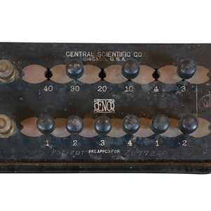 May include: A black metal box with a series of knobs and numbers. The box is labeled "CENTRAL SCIENTIFIC CO CHICAGO, USA" and "CENCO". The numbers on the box are 40, 30, 20, 10, 4, 3, 1, 2, 3, 4, 1, 2. The box also has the text "PS-EDT PALAPPED FOR 20772".