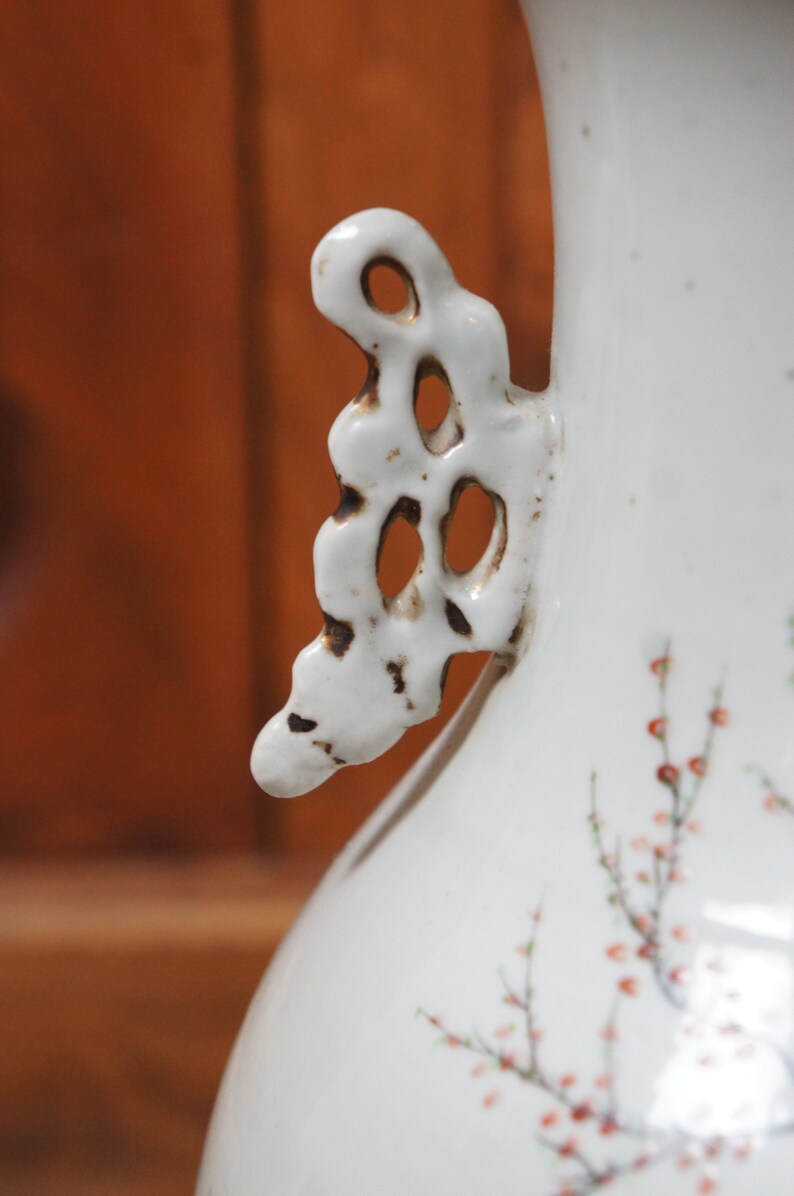 Op de afbeelding: Witte porseleinen vaas met een delicaat bloemenmotief en een decoratief handvat. Het handvat is opengewerkt en heeft een licht verweerde uitstraling.