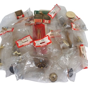 May include: A collection of vintage brass cabinet hardware in individual plastic bags. The hardware includes pulls, knobs, and hinges. The bags are labeled with the brand name "Mandell" and the words "Old Copper".