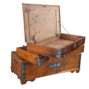 May include: A wooden storage chest with a hinged lid and two pull-out drawers. The chest is made of light brown wood with metal corner reinforcements and hardware. The lid is open, revealing the interior.