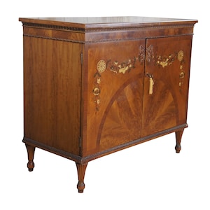 May include: A wooden cabinet with two doors, featuring intricate marquetry designs of flowers and butterflies. The cabinet has a dark brown finish and sits on four turned legs.
