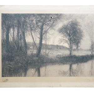 May include: A black and white landscape print featuring a serene waterside scene. Trees line the water's edge, with their reflections mirrored in the calm water. The print is framed with a white border, showing signs of age.