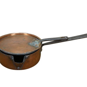 May include: A copper saucepan with a lid and a long, flat handle. The pan has a rounded body and a lid that fits snugly on top. The handle is made of a darker metal and is attached to the side of the pan.