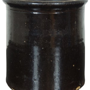 May include: A black glazed ceramic crock with a wide mouth and a rounded bottom. The crock has a slightly rough texture and a few small imperfections in the glaze.