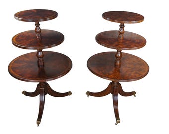 May include: Two three-tiered mahogany wood side tables with oval shaped tops and turned legs. The tables have a rich brown finish and brass feet.
