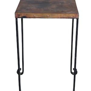 May include: A small, square copper-topped table with black metal legs. The table top has a distressed finish and is accented with copper rivets.