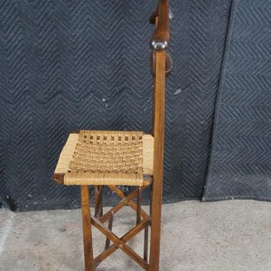 May include: A vintage wooden chair with a woven seat and a tall, curved backrest. The chair has a dark brown finish and a woven seat made of natural fibers. The legs are crossed for stability. The chair is designed for comfort and style.