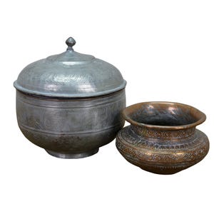 May include: Two antique metal vessels. One is a lidded, round container with etched floral designs and a small knob on top. The other is a smaller, open bowl with a decorative pattern around the rim and body. Both have a weathered appearance.