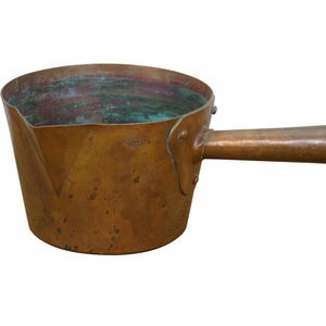May include: A copper saucepan with a long handle. The pan has a rounded body with a slightly angled rim. The handle is attached with rivets. The interior shows signs of oxidation, with green and red hues.