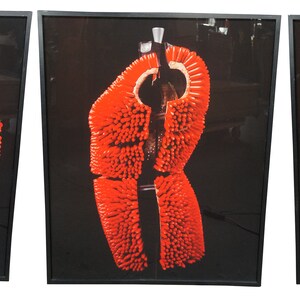 May include: Three framed photographs of a red, spiky, fabric-covered dress form. The dress form is in three different poses, showing the front, side, and back of the dress form.