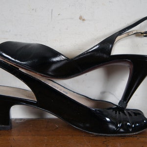 May include: Two pairs of black leather heeled slingback shoes. The top pair has a peep toe and a higher heel. The bottom pair has a closed toe and a lower heel.
