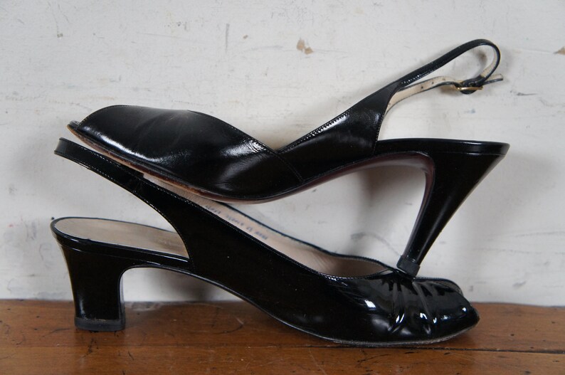 May include: Two pairs of black leather heeled slingback shoes. The top pair has a peep toe and a higher heel. The bottom pair has a closed toe and a lower heel.