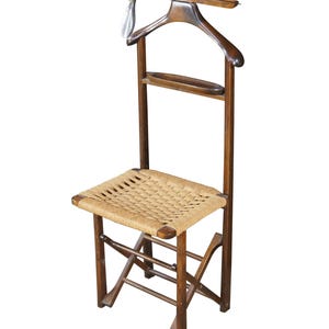 May include: A vintage wooden valet chair with a woven seat. The chair features a built-in hanger and a small shelf. The wood has a warm, brown tone, and the seat is made of a light-colored woven material.