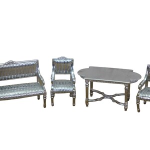 May include: A miniature silver-colored furniture set consisting of a sofa, two armchairs, and a rectangular table. Each piece features ornate carved detailing on the legs and backrests, with a metallic finish and a textured surface pattern.