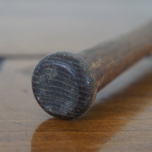 May include: Close-up of the end of a wooden baseball bat. The bat is brown and has a dark brown, slightly worn finish.