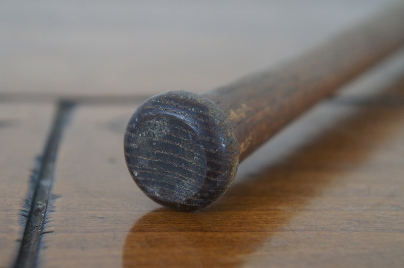 May include: Close-up of the end of a wooden baseball bat. The bat is brown and has a dark brown, slightly worn finish.