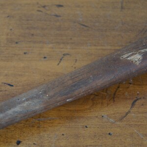May include: A close-up of a wooden baseball bat with a worn surface and a small chip in the wood.