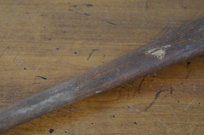 May include: A close-up of a wooden baseball bat with a worn surface and a small chip in the wood.