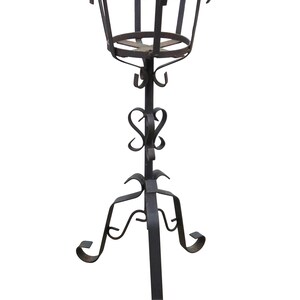 May include: A dark brown wrought iron plant stand featuring a circular basket top with four curved hooks, a central vertical rod with decorative scrollwork, and a tripod base with three legs that terminate in outward-curving feet.