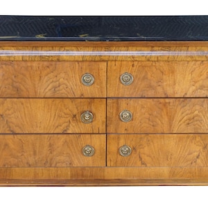 May include: A wooden dresser with six drawers, featuring a black marble top and brass hardware. The dresser has a light brown finish with dark accents and curved black side supports. The design is classic and elegant.