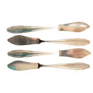 May include: Four silver butter knives with ornate handles, arranged in a row on a white background.