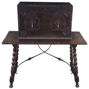 May include: A dark wood antique cabinet with intricate metalwork and brass hardware sits atop a table with twisted wooden legs and iron supports.