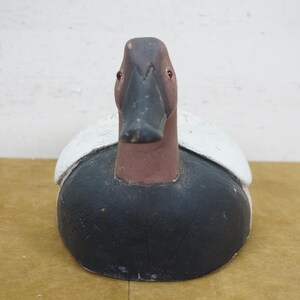 May include: A wooden duck decoy with a black body, brown head, and white accents on the wings. The decoy has a detailed beak and red eyes, and is designed to attract real ducks. This decorative item is a classic piece of Americana.