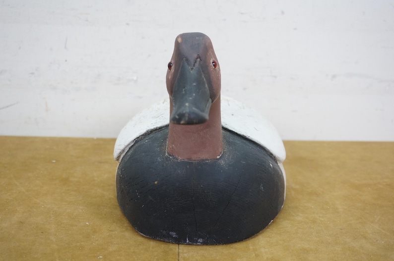 May include: A wooden duck decoy with a black body, brown head, and white accents on the wings. The decoy has a detailed beak and red eyes, and is designed to attract real ducks. This decorative item is a classic piece of Americana.
