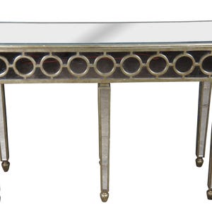 May include: A mirrored console table with a rectangular top and a decorative front featuring circular cutouts. The table has four slender, mirrored legs with gold-toned accents. The frame is a metallic gold color.